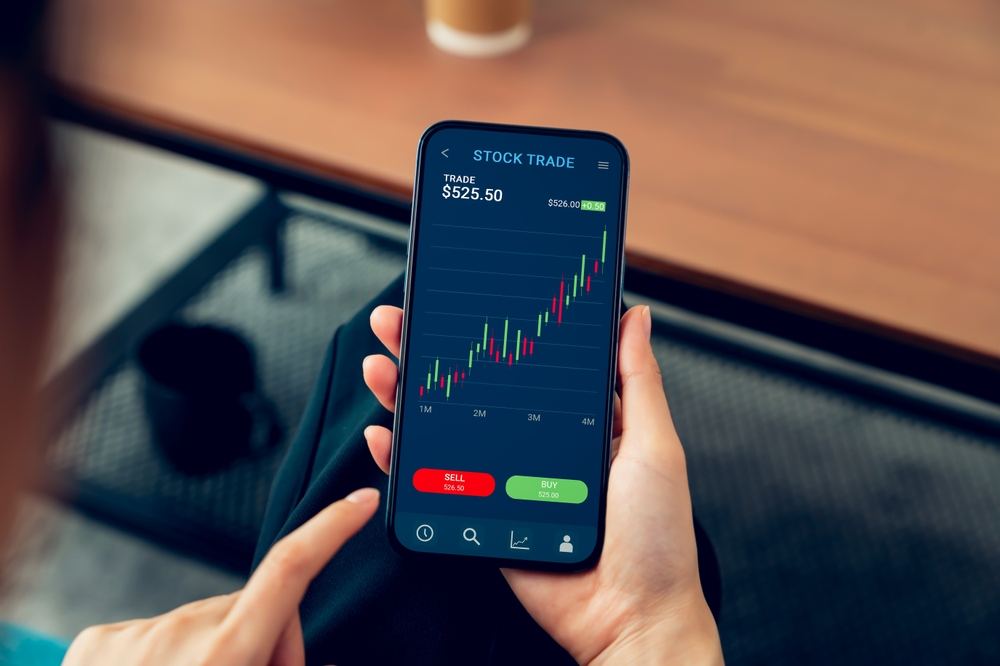 BusinessmanTraderUsingSmartphoneWithStockMarketInvestmentsAndGraph